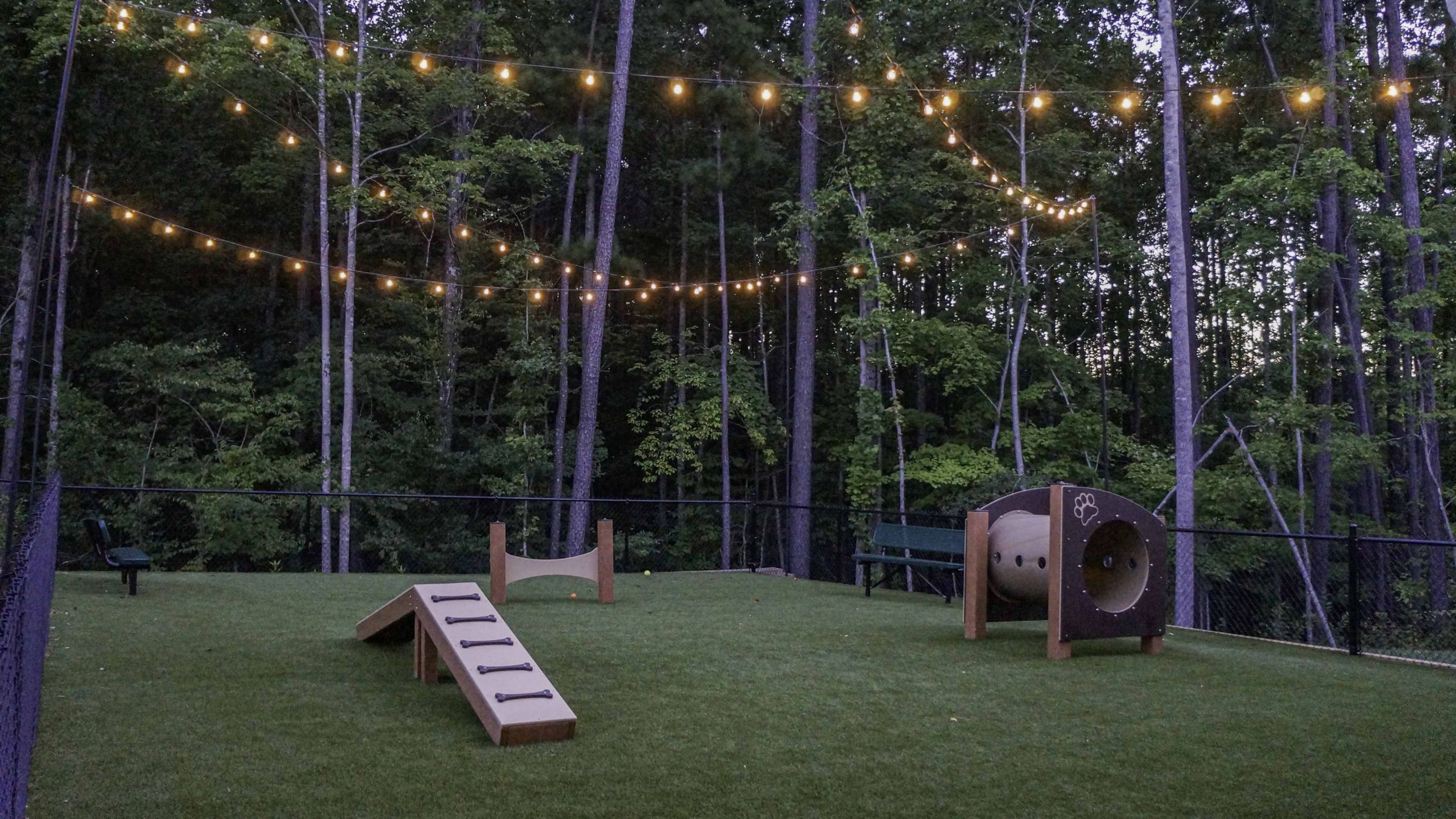 Hawthorne at Parkside outdoor dog park with agility equipment at twilight with pretty lights overhanging the area